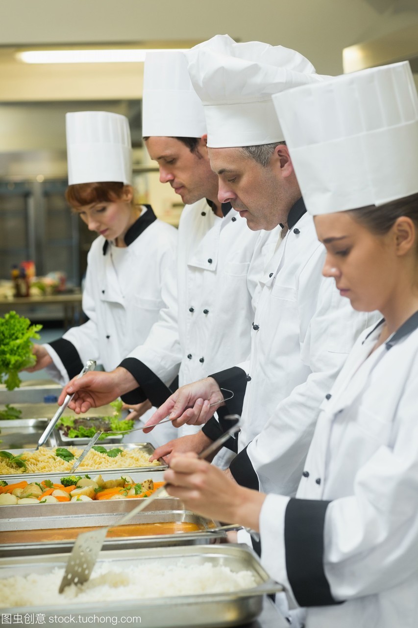 四个厨师在忙碌的厨房里服务托盘